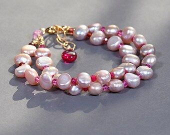 Puede incluir: Un collar de perlas de doble cadena con detalles en rosa y dorado. El collar presenta perlas rosas y pequeñas piedras preciosas rosas.