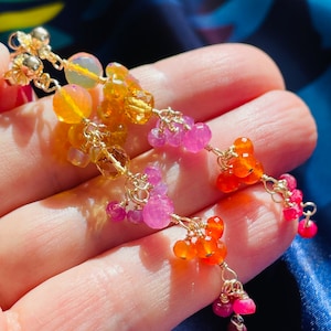 Può includere: Una catena d'oro con un gruppo di pietre preziose arancioni, rosa e rosse. La catena è realizzata con piccoli e delicati anelli e le pietre preziose sono disposte a cascata.