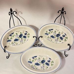 May include: Three oval-shaped ceramic bowls with a cream-colored base and a blue rim. The interior of each bowl features a floral pattern with dark blue poppies, light blue blossoms, and green foliage on a white background.