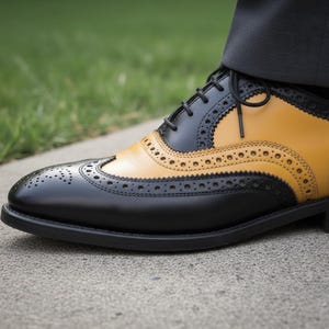 K&ouml;nnte beinhalten: Nahaufnahme eines zweifarbigen Lederschuhs. Der Schuh hat eine schwarze Basis mit einem senfgelben Oberteil. Der Schuh hat dekorative Perforationen und schwarze Schn&uuml;rsenkel. Der Schuh steht auf einer Betonoberfl&auml;che.