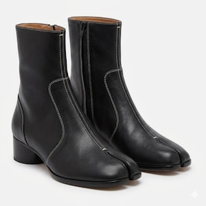 May include: A pair of black leather ankle boots featuring a distinctive split-toe design, white contrast stitching along the seams, a side zipper closure, and a low cylindrical block heel. The boots have a smooth finish and a mid-calf height.
