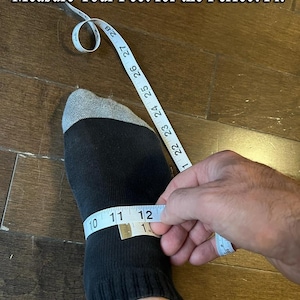 May include: A black sock with a gray top is being measured with a white measuring tape. The tape reads 10, 11, and 12 inches. The text "Measure Your Feet for the Perfect Fit" is at the top of the image.