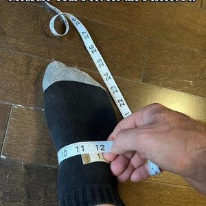 Puede incluir: Un calcet&iacute;n negro con la parte superior gris se mide con una cinta m&eacute;trica blanca. La cinta m&eacute;trica indica 25,4, 27,9 y 30,5 cm. El texto "Measure Your Feet for the Perfect Fit" est&aacute; en la parte superior de la imagen.
