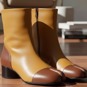 May include: A pair of two-tone leather ankle boots. The boots feature a tan upper with a brown toe cap and heel. A zipper runs along the side of each boot. The boots have a low, black heel.
