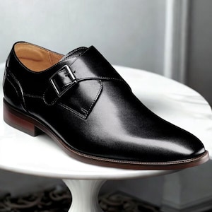 May include: A black leather monk strap shoe with a silver buckle. The shoe has a brown sole and a smooth, polished finish. The shoe is a classic style, suitable for formal occasions.