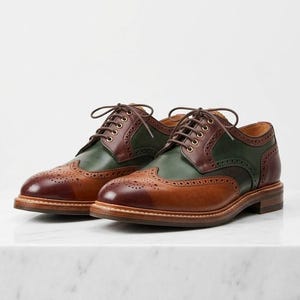 May include: A pair of lace-up oxford shoes featuring a wingtip design with decorative brogue perforations. The shoes are constructed with a combination of tan, dark brown, and forest green leather panels, finished with brown laces and a stacked heel.