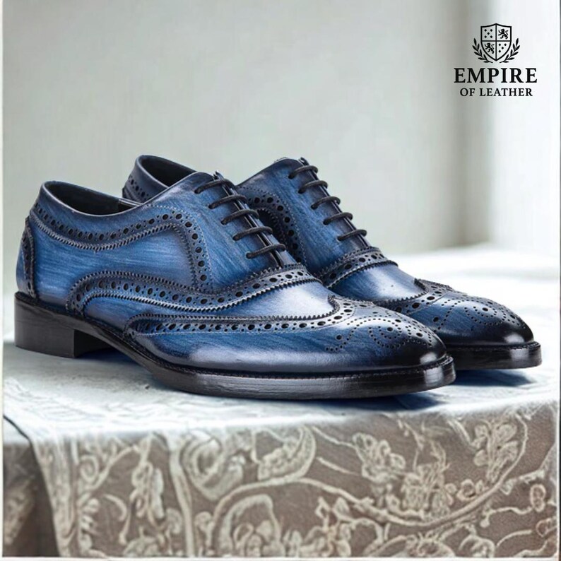 May include: A pair of blue leather brogue shoes with black laces. The shoes have a distressed finish and decorative perforations. The image includes the text "EMPIRE OF LEATHER" and a crest logo.