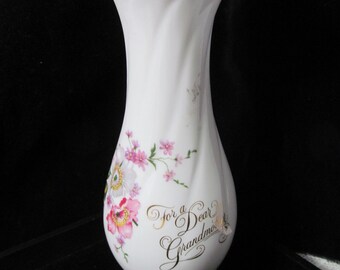 May include: White ceramic vase with a gold rim and floral design. The vase has a gold inscription that reads "For a Dear Grandma".