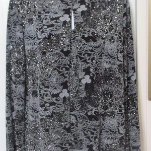 May include: Black long-sleeve top with a mandarin collar and floral pattern. The top is embellished with silver sequins, creating a shimmering effect. The design features a button closure down the front.