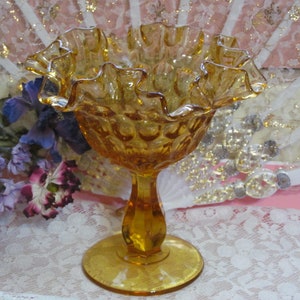 May include: A vintage amber glass candy dish with a ruffled rim and a pedestal base. The dish has a textured surface and is perfect for displaying small treats or trinkets.