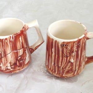 May include: Two ceramic mugs with brown and white woodgrain designs. The mugs have a handle on the right side and are sitting on a white surface.