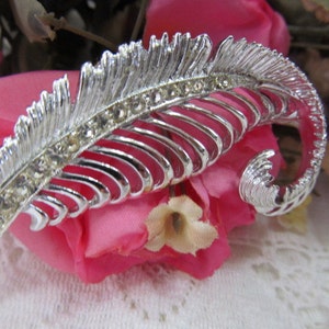 May include: A silver feather-shaped brooch with a row of clear rhinestones.