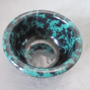 May include: A small, round bowl with a glossy finish. The bowl's exterior features a striking pattern of teal and black, creating a marbled effect. The interior is a solid, reflective black. The bowl is likely made of ceramic or a similar material.