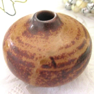 May include: A small, round ceramic vase with a narrow opening. The vase has a speckled, earthy brown and reddish-brown pattern. The vase is a decorative item.