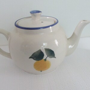 May include: White ceramic teapot with a blue and white trim and a lemon design. The teapot has a lid and a spout.