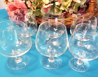 May include: A set of five clear glass snifters, each featuring a delicate etched wheat pattern on the bowl. These short-stemmed glasses have a rounded shape and a wide base, designed for serving spirits or brandy in a clear, transparent finish.