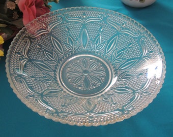 May include: A clear glass serving bowl with a decorative, embossed pattern. The bowl has a scalloped edge and a raised center.