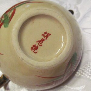 May include: A beige ceramic teapot with red and green floral designs. The bottom of the teapot has a red stamp that reads "華麗" in Japanese.