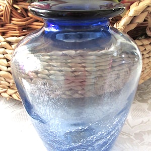 May include: A cobalt blue glass vase with a textured, crackled finish. The vase has a wide mouth and a rounded body.