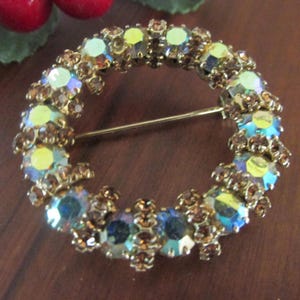 K&ouml;nnte beinhalten: Vintage, kreisf&ouml;rmige Brosche mit goldfarbenem Metallrahmen. Die Brosche ist mit schillernden, mehrfarbigen Strasssteinen in Blau-, Gelb- und Braunt&ouml;nen verziert. Ein klassisches Schmuckst&uuml;ck.