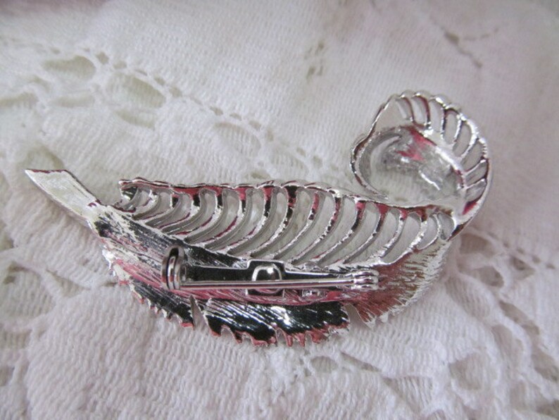 May include: Silver tone feather brooch with a detailed design and a pin closure.