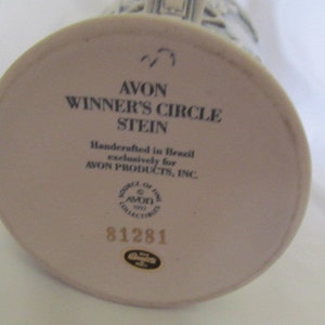 May include: White ceramic stein with a black and white image of a building. The bottom of the stein has the text "AVON WINNER'S CIRCLE STEIN" and "Handcrafted in Brazil exclusively for AVON PRODUCTS, INC." along with a logo and the number 81281.