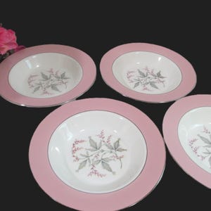 May include: Four round soup bowls with a wide pink rim and a silver-toned edge. The center of each bowl is white and features a botanical illustration of gray leaves and small pink flowers. The bowls are arranged in a group on a dark surface.