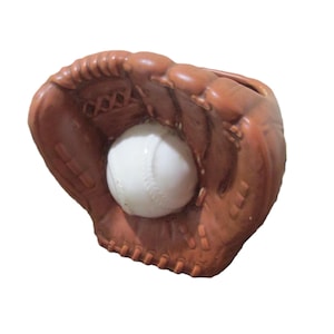 May include: A brown baseball glove with a white baseball inside. The glove is made of leather and has visible stitching. The baseball has red stitching. The image is set against a white background.