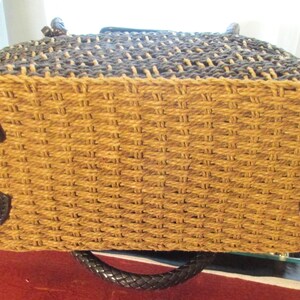 May include: Woven tote bag with a two-tone design. The top section is dark brown, and the bottom is tan. The base features four black heart-shaped accents. The bag has a black braided handle.