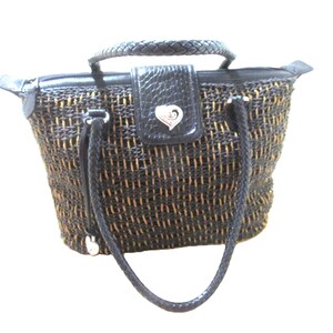 May include: A woven tote bag with a black and tan pattern. The bag has a braided top handle and a black leather flap with a silver heart-shaped emblem. Black braided straps connect to the bag's sides.