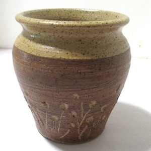 May include: A handcrafted ceramic vase with a speckled tan rim and a dark brown body. The vase features a band of brown and is adorned with etched floral designs. The vase is approximately 6 inches tall and 5 inches wide.