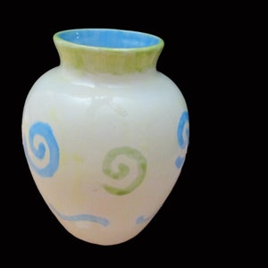 May include: A white ceramic vase with a blue and green swirl design. The vase has a rounded body and a wide mouth.
