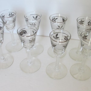 May include: Set of eight clear glass cordial glasses. Each glass features a silver rim and leaf design. The glasses have a long stem and a round base. Ideal for serving after-dinner drinks.