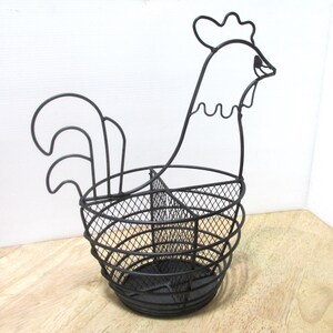 May include: Black metal rooster-shaped basket. The basket features a wire mesh design for the body and a detailed rooster head and tail. The basket is designed to hold items and is suitable for kitchen or home decor.