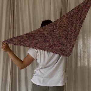 May include: A triangular hand-knitted shawl featuring a variegated color palette of muted pinks, purples, and earthy browns. The accessory is crafted with a fine yarn texture, displaying a consistent stockinette stitch pattern throughout the fabric.