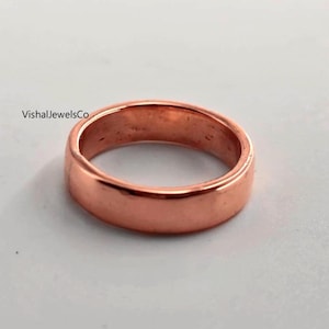May include: A copper-colored ring with a smooth, polished surface. The ring is a simple band design, with a rounded profile. The text "VishalJewelsCo" is visible on the upper left side of the image.