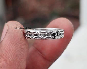 May include: A silver ring with a detailed woven pattern. The ring is held in a person's hand, showcasing the intricate design. The ring's surface reflects light, highlighting the texture. The ring is a piece of jewellery.