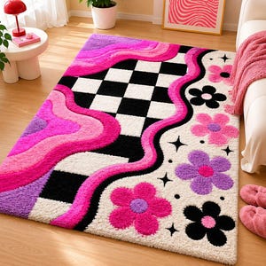 May include: A rectangular area rug featuring a black and white checkered pattern on one side and a cream-colored background on the other. The design includes wavy bands of hot pink and purple, accented with black, pink, and purple flower motifs.