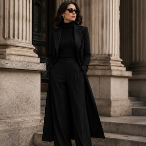 May include: A black ensemble consisting of a long coat, a turtleneck sweater, and wide-leg trousers. The outfit is paired with dark-tinted sunglasses. The clothing features a solid black color palette with structured tailoring and clean lines.