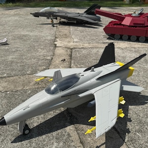 May include: A collection of toy military vehicles, including a gray and black jet fighter with yellow accents and missiles, a dark gray jet, and a red tank with a long cannon.