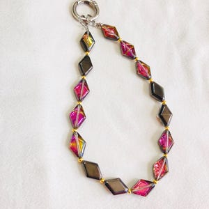 May include: A keychain with a silver clasp and a chain of iridescent, diamond-shaped beads in shades of pink, gold, and gray. The beads are strung together with small gold-colored beads.