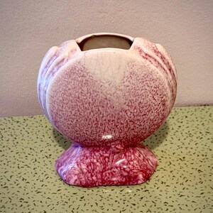 May include: A decorative ceramic vase with a bulbous body and a flared base. The vase is primarily a speckled burgundy color with white accents and a smooth, glossy finish. The opening is a contrasting neutral color.
