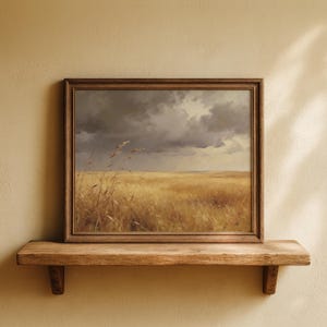 Könnte beinhalten: Gerahmtes Landschaftsgemälde, das ein Weizenfeld unter einem dramatischen, bewölkten Himmel zeigt. Das Kunstwerk zeigt eine Palette aus Goldgelb, Braun und Grau, mit einem Holzrahmen. Das Gemälde wird auf einem Holzregal ausgestellt.