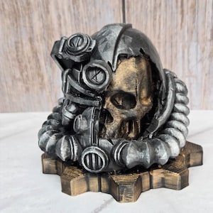 May include: A detailed, steampunk-style skull sculpture. The skull is partially encased in a metallic helmet with intricate gears and gauges. The base is a gear shape, and the skull has a gold-colored interior.