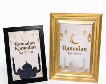 May include: Two framed prints with a Ramadan theme. One frame is black, the other is gold. Both feature the words "Ramadan Kareem" and a mosque silhouette. The gold frame has a textured design.