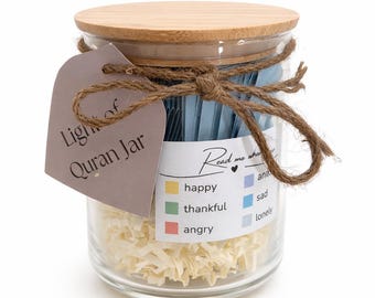 May include: A glass jar with a wooden lid and a decorative twine bow. The jar contains blue slips of paper and shredded paper. A tag reads "Light of Quran Jar" and a label lists emotions: happy, thankful, angry, sad, and lonely.