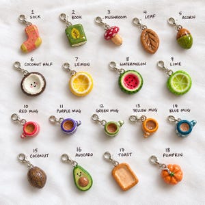 May include: A collection of eighteen miniature charms with silver-tone lobster clasps, featuring various shapes including a sock, book, mushroom, leaf, acorn, coconut half, lemon, watermelon, lime, mugs, coconut, avocado, toast, and pumpkin.