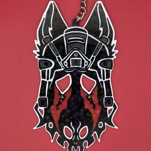 May include: Black and white keychain featuring a stylized wolf head design with a red and black pattern. The keychain has a silver keyring and chain, set against a red background. The wolf head has a unique, geometric design.