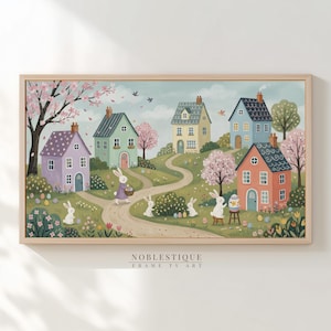 Può includere: Una stampa incorniciata con una scena pasquale stravagante. Case dai colori pastello punteggiano una collina, con coniglietti, uova e alberi in fiore. L'opera d'arte ha una cornice in legno chiaro e il testo "NOBLESTIQUE FRAME TV ART" in basso.