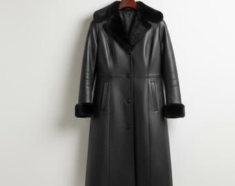 May include: A long, black leather coat with a faux fur collar and cuffs hangs from a wooden hanger. The coat features a button-down front and a tailored silhouette, offering a classic and elegant look. The coat is designed for cold weather.